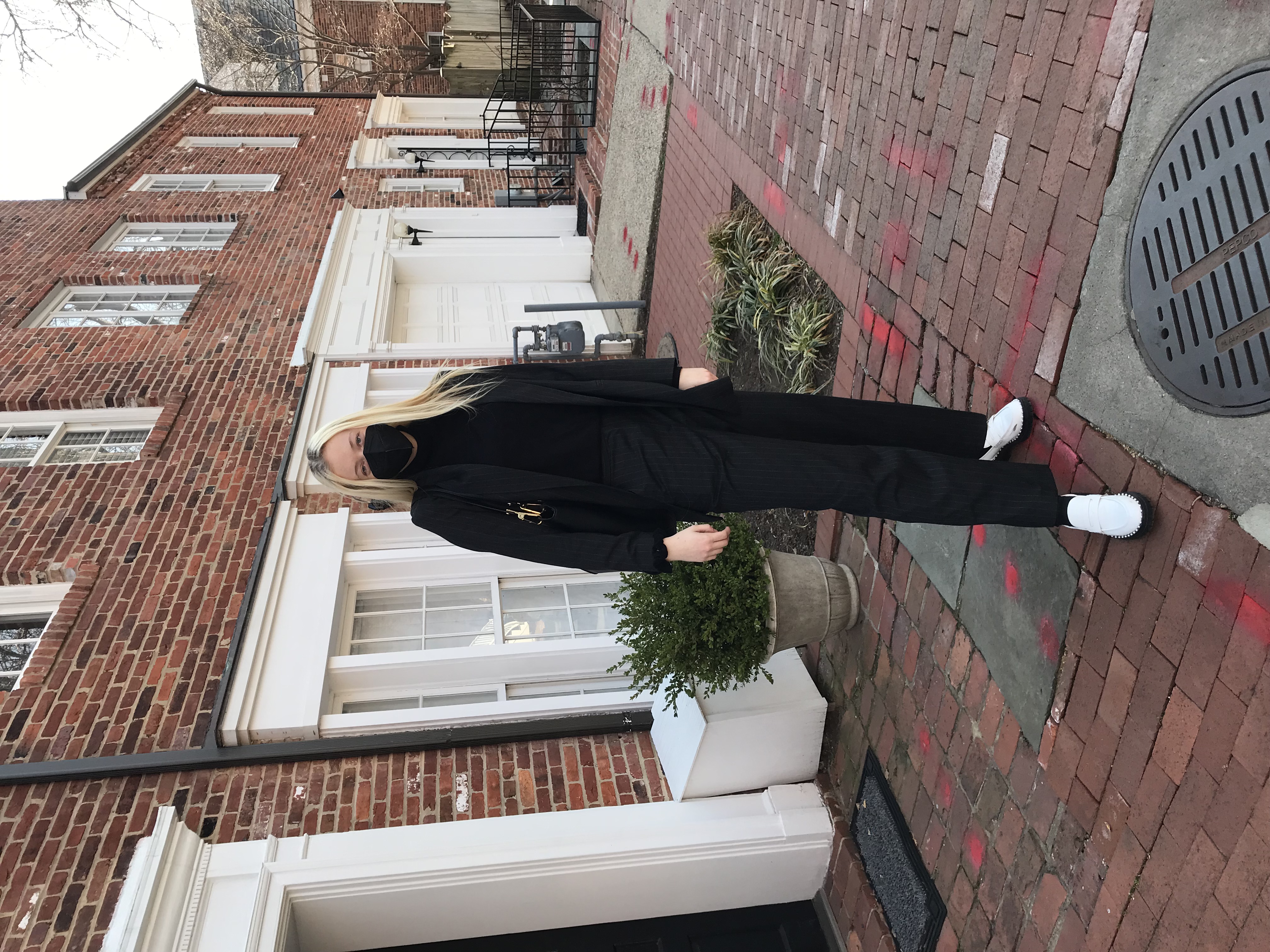 Layla Mitchell dressed all in black posing in front of some brick buildings. 