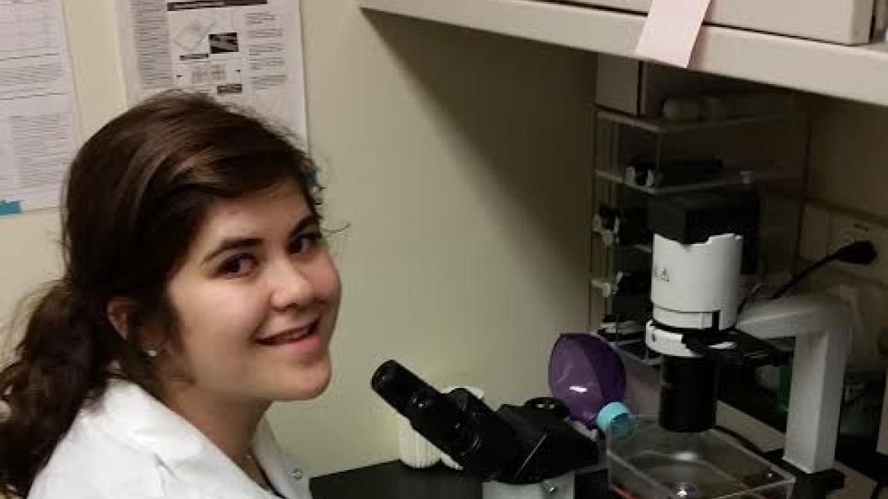 Mor Alkaslasi in a lab coat conducting an experiment using a microscope. 