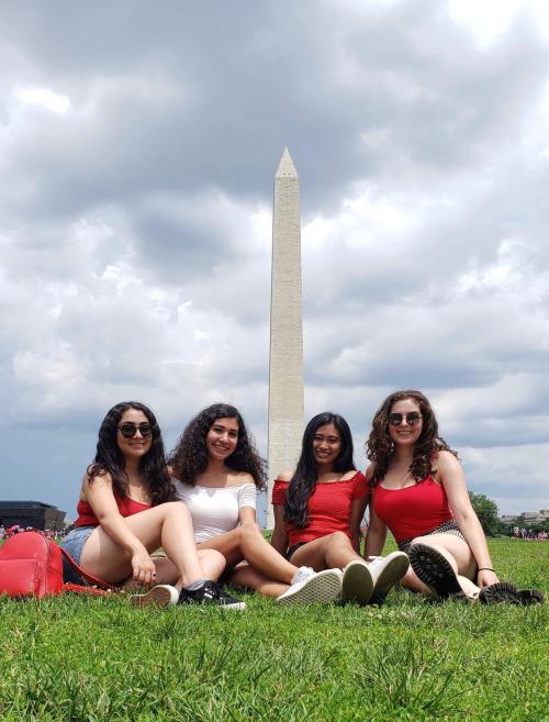 Alina sitting with 3 friends on the grass in front of the Washington Monument.